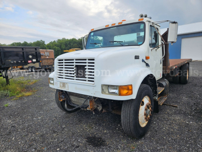International 4900 flatbed dump truck in a yard, front grill, dual rear wheels, white cab, flatbed in back, stock photo watermark
