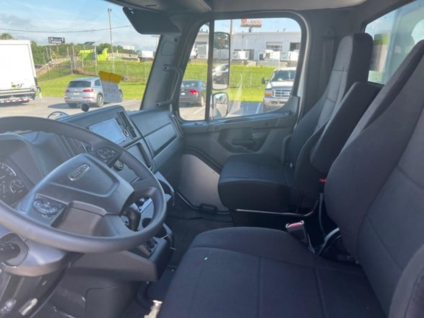 Driver and passenger seats in Freightliner M2 106 Plus cab interior with dashboard and steering wheel.