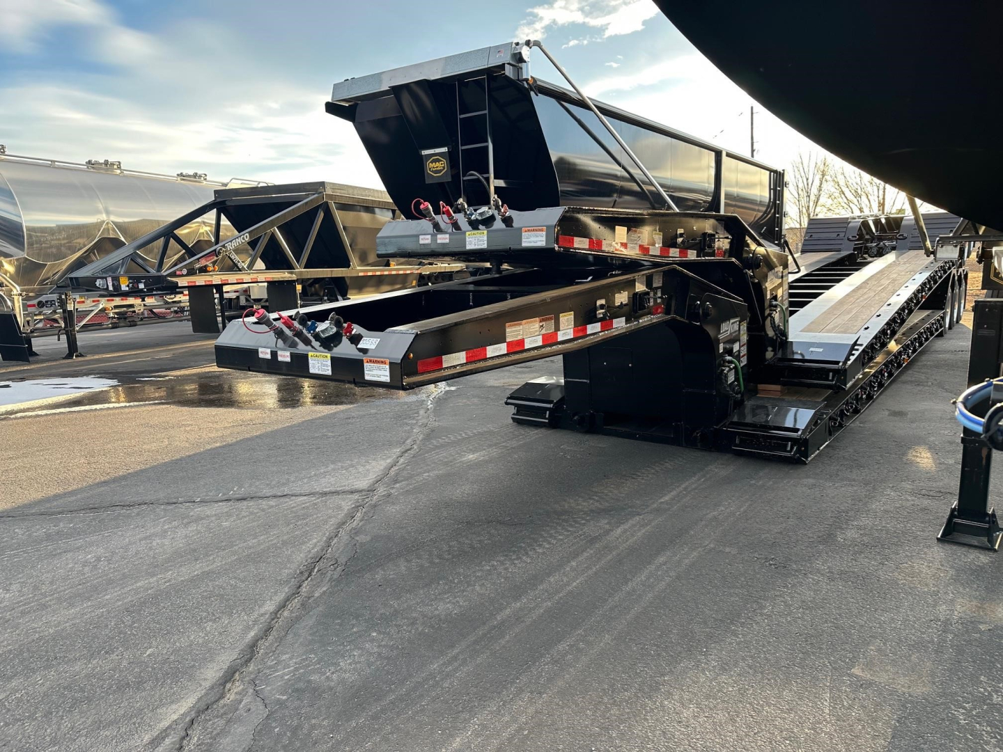 Load King lowboy trailer with hydraulic ramps and gooseneck, side rails and reflective tape. New trailer in a lot with other trailers visible.