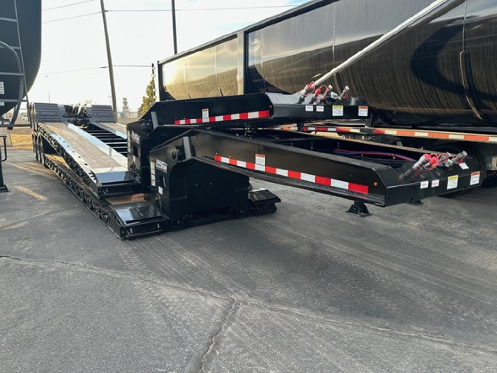 Lowboy trailer by Load King Ss showing gooseneck area and deck with black frame, red/white reflective strips, and hinged ramps.