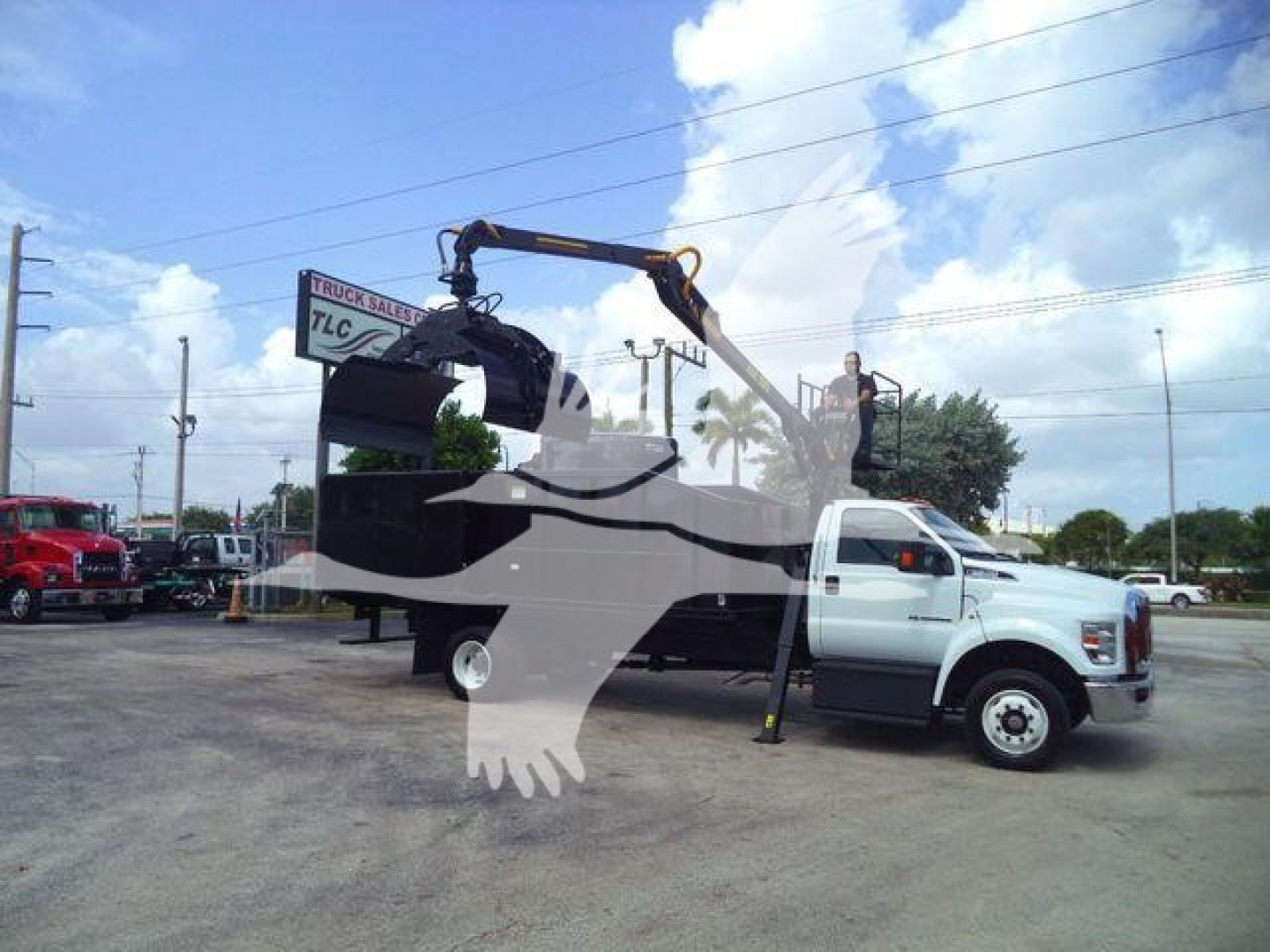 2023 Ford F650 truck with grapple arm lifting a large bucket attachment, white cab, black grapple with view of yard in background.