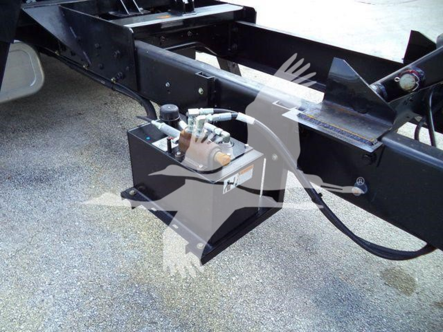 Hydraulic reservoir and control components mounted on a truck chassis frame showing hydraulic lines and actuator box.