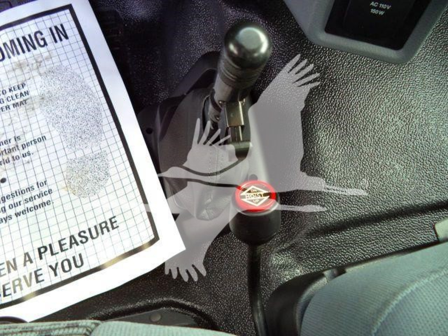 Interior view showing gear shifter and ignition area of a 2023 Ford F650 grapple truck, with a paper document on the left and a red cap label on a component.