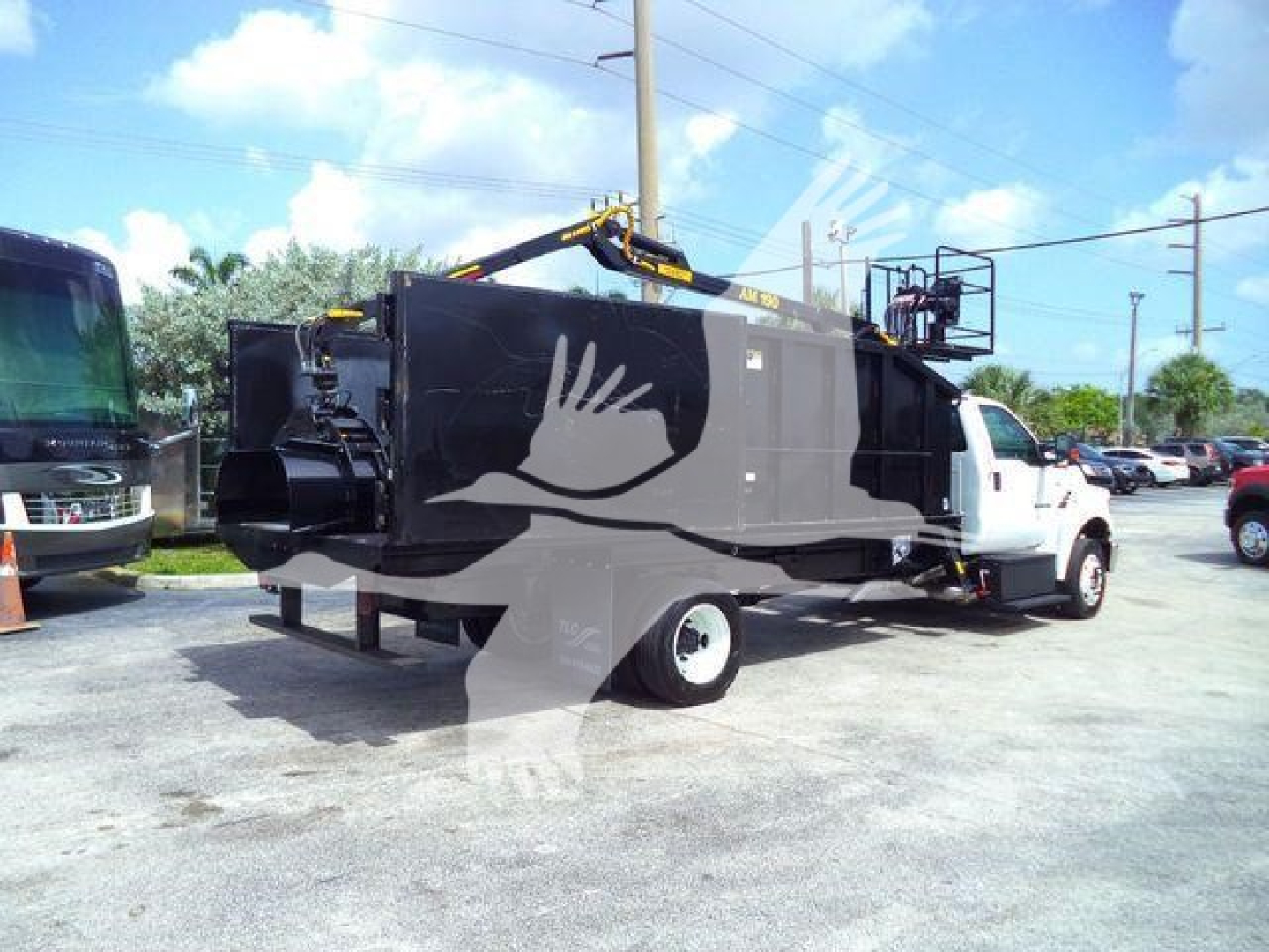 Truck-mounted grapple unit on a white cab and chassis, black rear body with hydraulic arm and warning decals visible; side view showing grapple area and rear exhaust.