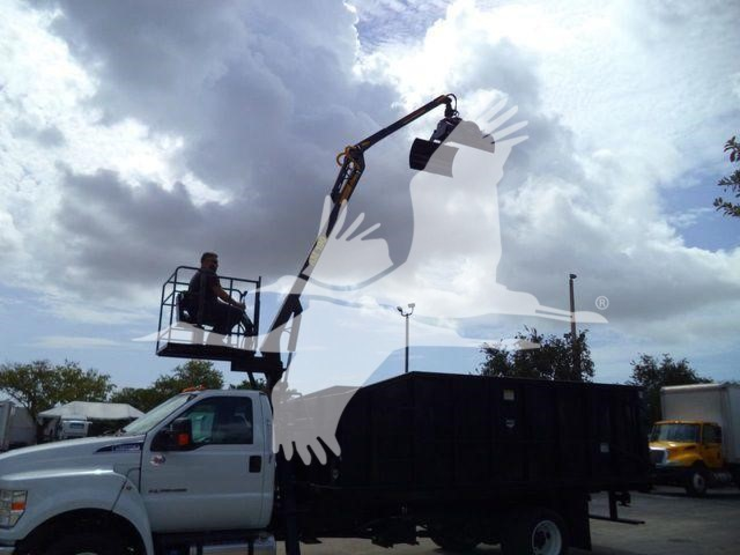 Truck bed with mounted grapple arm in operation; side view of a white Ford F-650 dump truck with crane attachment and operator platform.