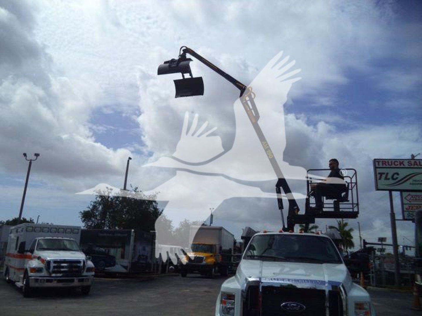Ford truck with a hydraulic grapple attachment on a high-arm crane in a truck lot. Visibility of nearby trucks and signs in background.