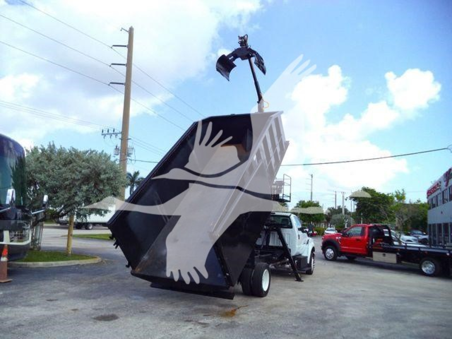 Front-left view of a 2023 Ford F650 grapple truck with a large black grapple bucket raised, white cab and black chassis, in a dealership lot.