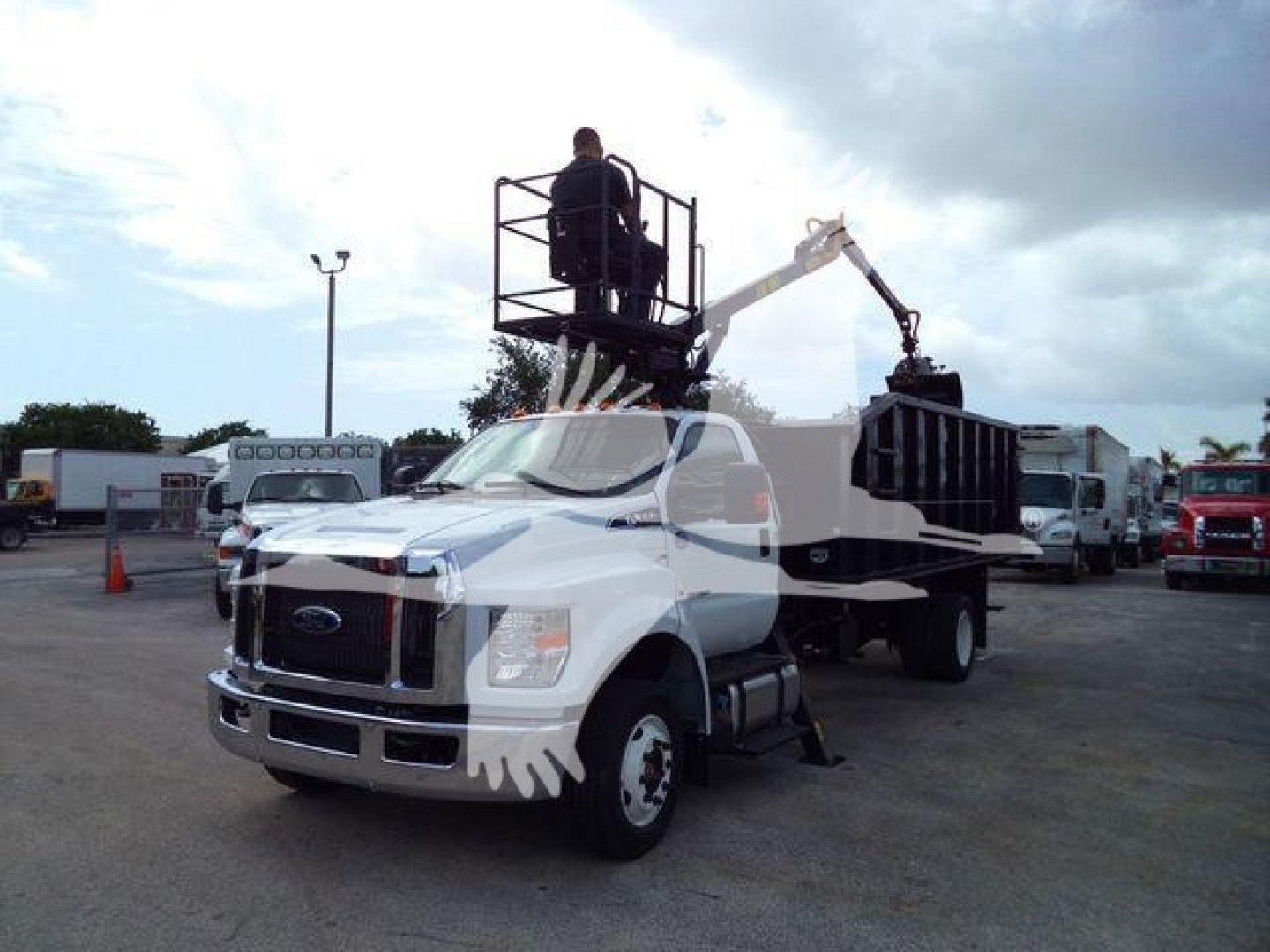 Flatbed tow truck with a hydraulic lift and elevated worker basket on a Ford F-650 chassis, white cab, grapple equipment in a dealership lot.