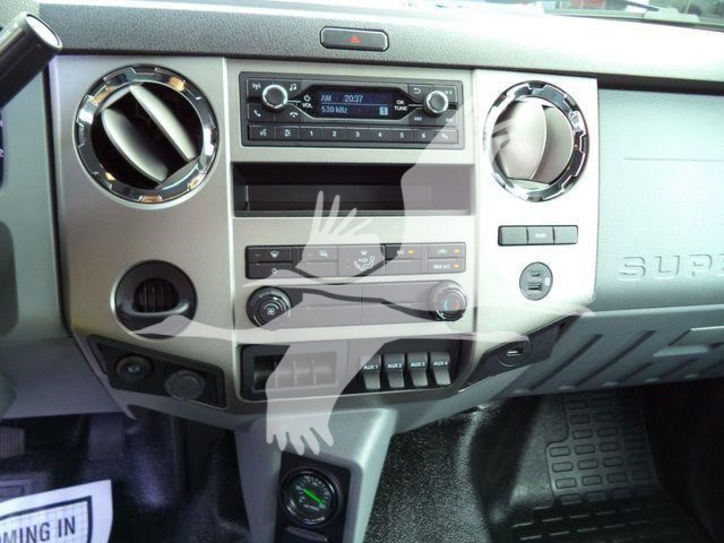 Truck dashboard center console with circular vents, radio head unit, climate controls, and several switches. Center area shows blank area with hand watermark; no legible model text besides generic dashboard layout.