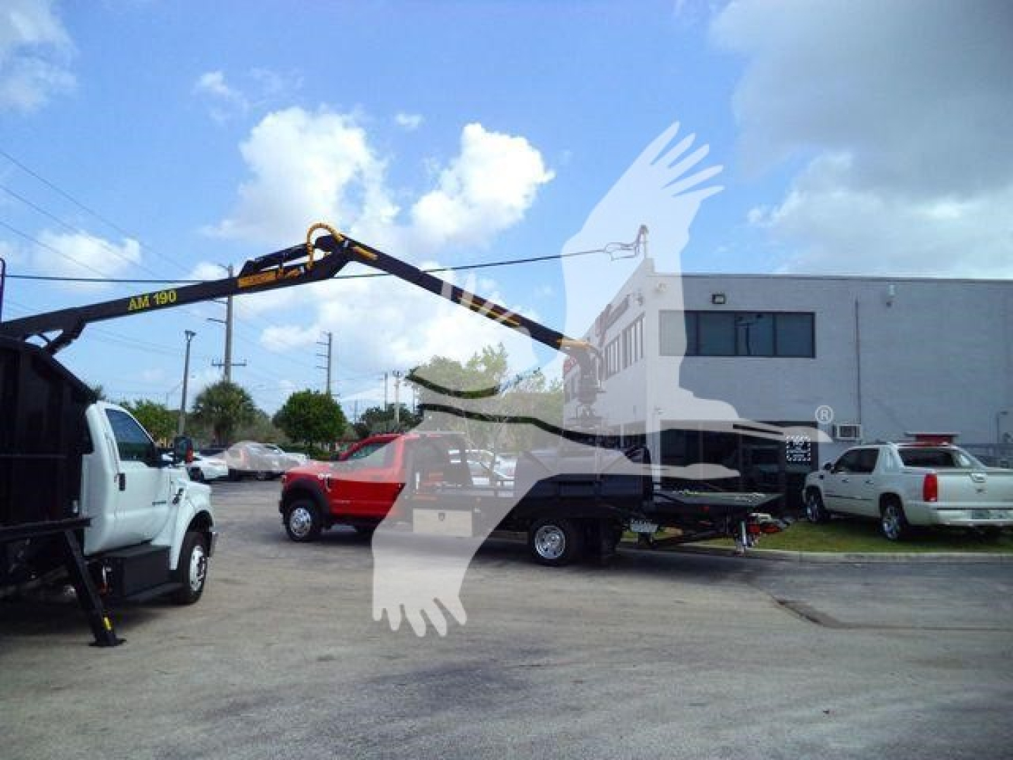 Ford F650 grapple truck in a dealership lot with a hydraulic arm extended; visible text on the arm shows AM190; other vehicles parked nearby.