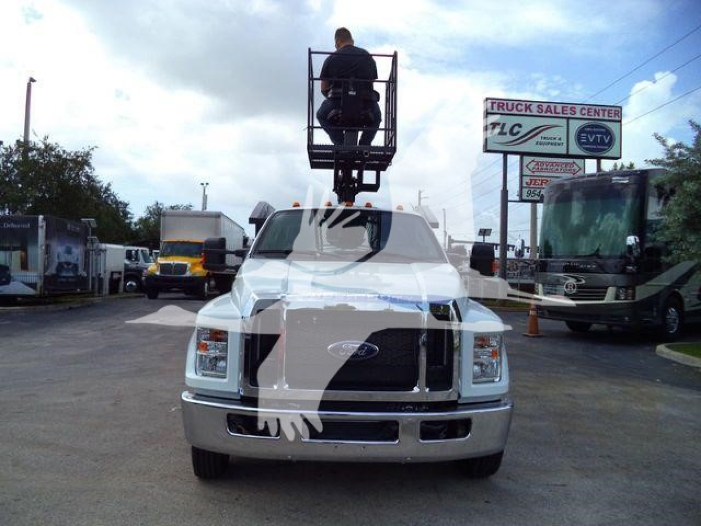 Front view of a 2023 Ford F-650 SD grapple truck with a raised operator platform on the cab and a grappling arm on top, in a dealership lot.