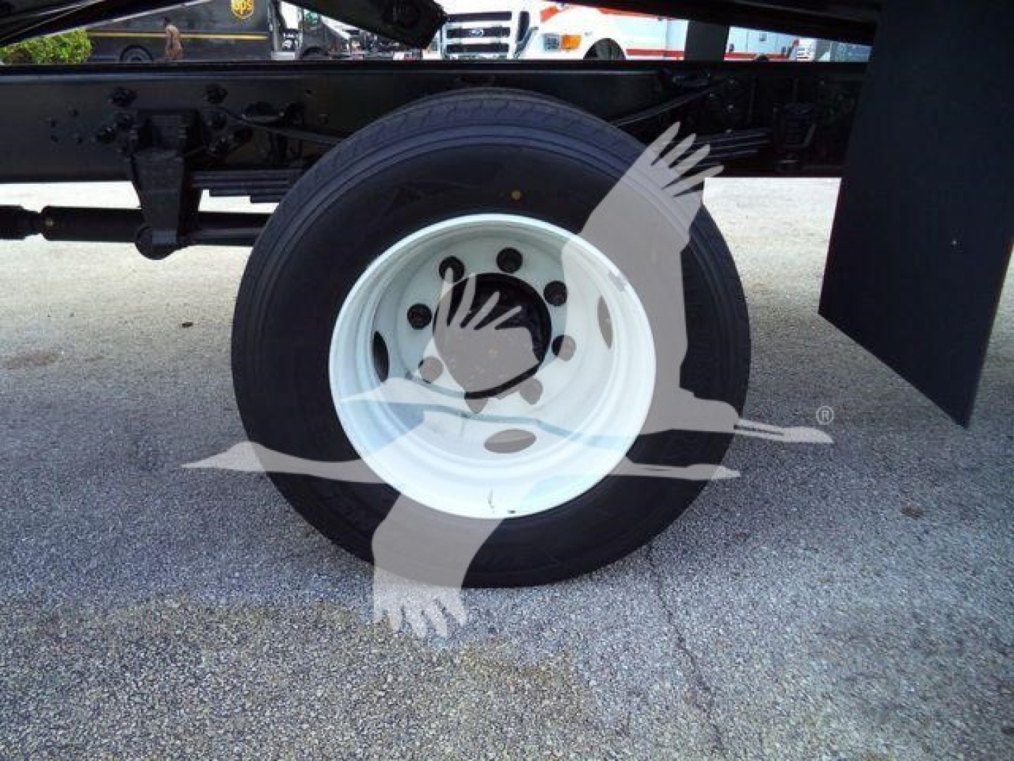 Truck wheel with white steel rim and tire, undercarriage visible on a flatbed truck chassis.