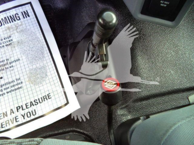 Interior view showing gear shifter and ignition area of a 2023 Ford F650 grapple truck, with a paper document on the left and a red cap label on a component.