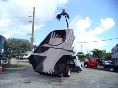 Front-left view of a 2023 Ford F650 grapple truck with a large black grapple bucket raised, white cab and black chassis, in a dealership lot.