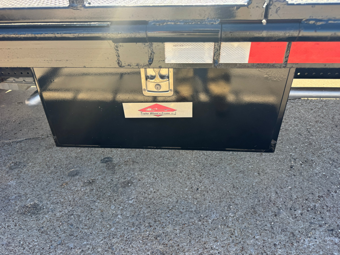 Isuzu NPR-HD flatbed truck rear showing black toolbox under-bed storage and reflective tape