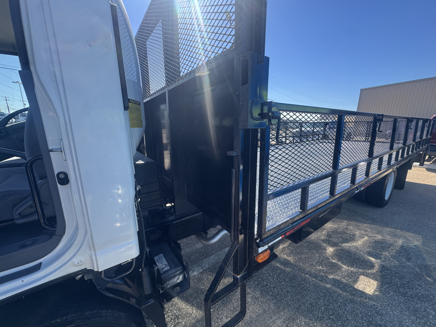 Isuzu NPR-HD flatbed truck side view showing entry step and metal stake bed with mesh sides.