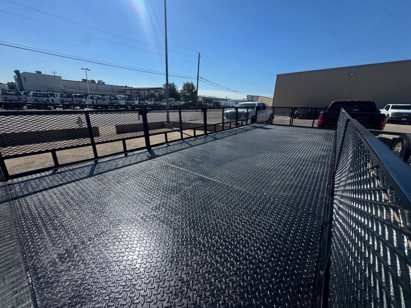Isuzu NPR-HD flatbed truck bed with diamond plate surface and side rails, urban lot background.