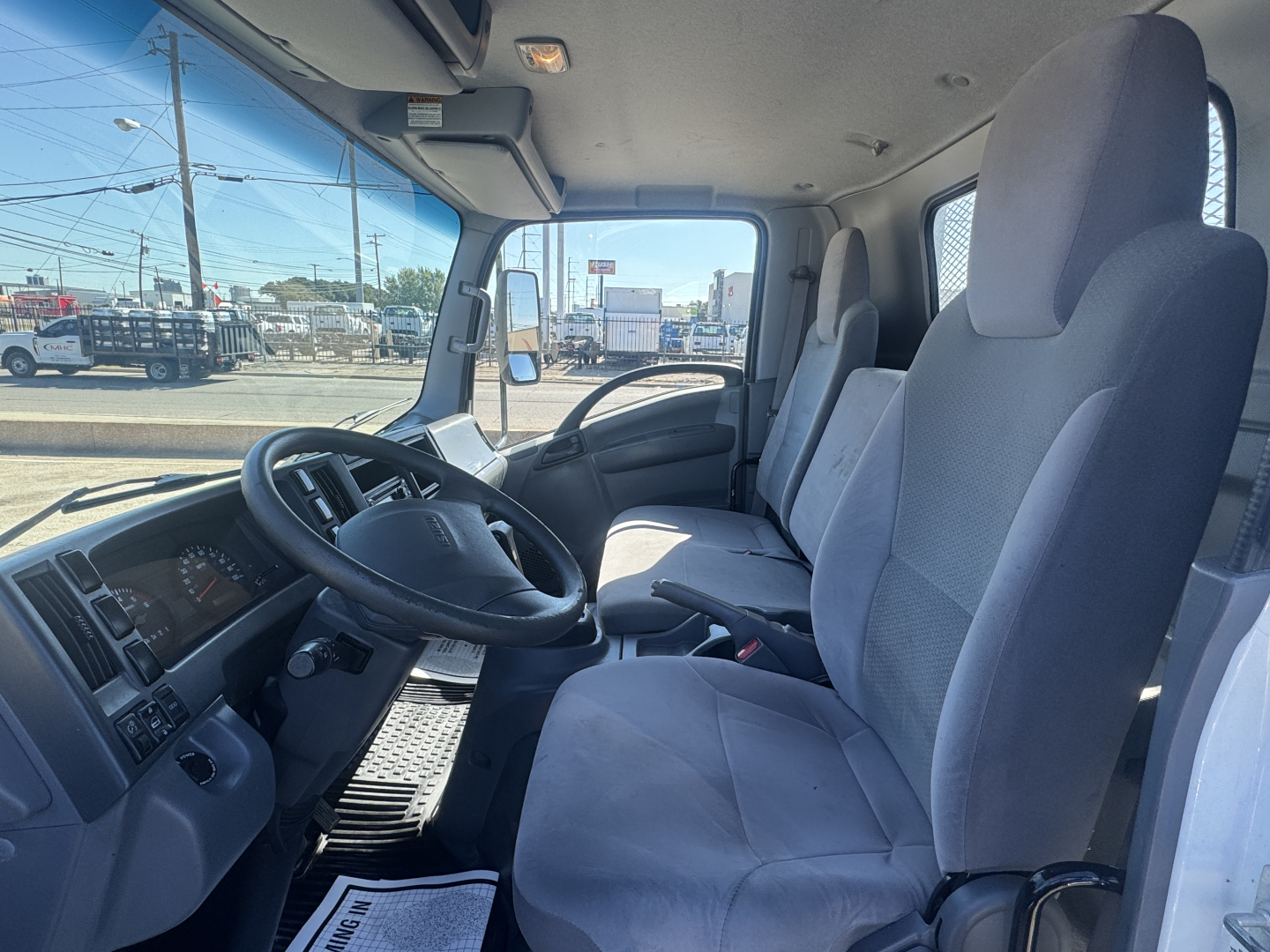 Isuzu NPR-HD truck interior showing driver seat and passenger seat with steering wheel and dashboard visible.
