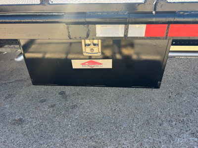 Isuzu NPR-HD flatbed truck rear showing black toolbox under-bed storage and reflective tape