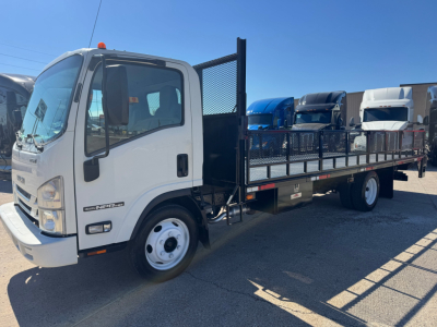 Isuzu NPR-HD flatbed truck with cab and long metal flatbed, black mesh divider behind cab, white cab, stock number plate visible on door, blue and white trucks in background.