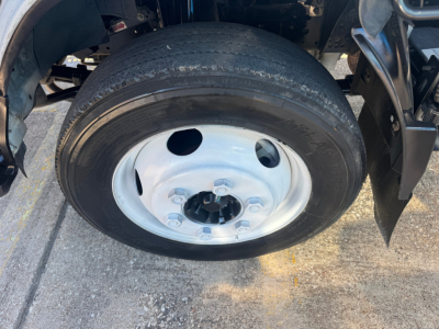Isuzu NPR-HD wheel and tire close-up showing steel rim, five lug nuts, and hub area.