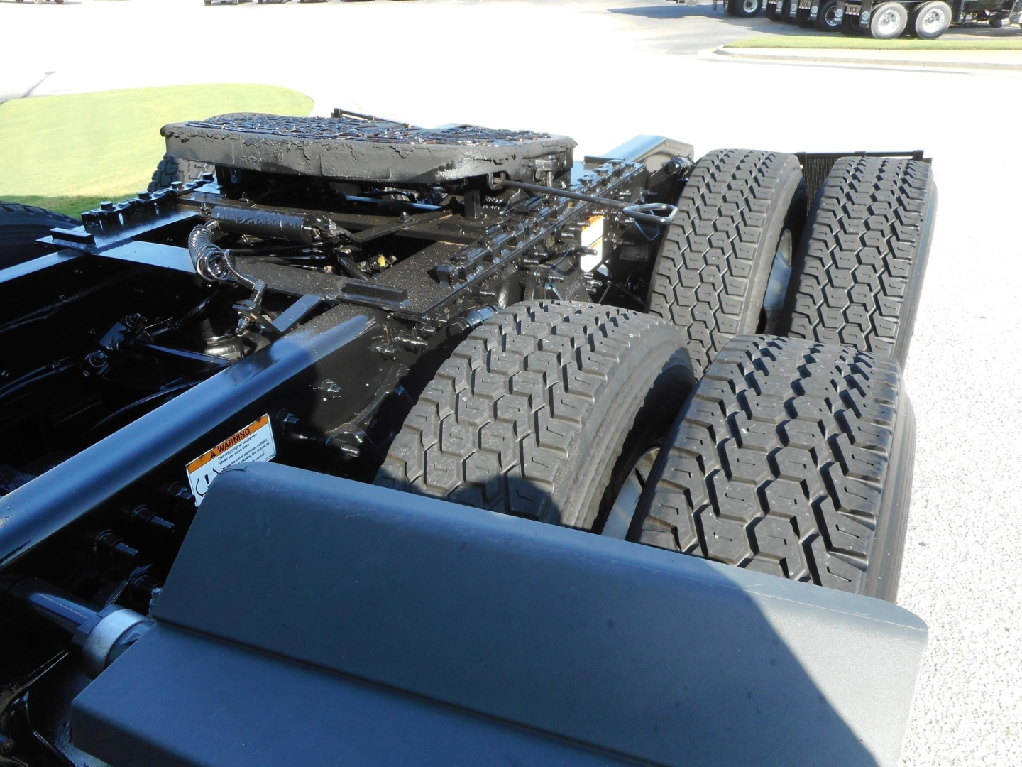 Tractor truck chassis with dual rear axles and tires; visible metal framework and fifth-wheel area. No legible labels clearly visible in foreground.