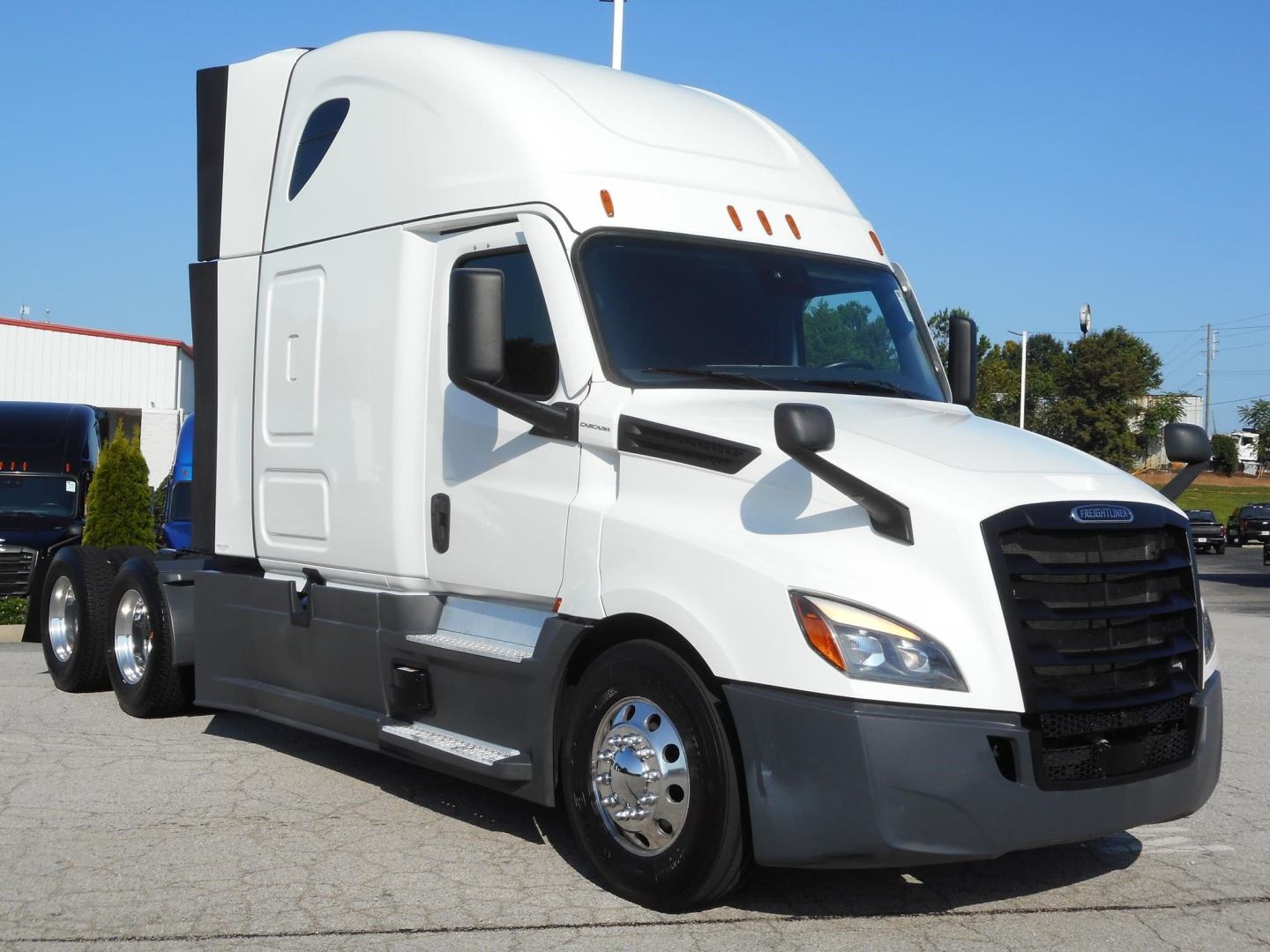 Freightliner Cascadia 126 sleeper cab tractor, white exterior, side cab mirrors, aerodynamic headlights, grille, chrome fuel tanks, aluminum wheels; truck in daylight.