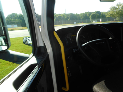 Truck cab interior view of a Freightliner Cascadia, steering wheel visible, dashboard and driver seat, yellow grab handle near door
