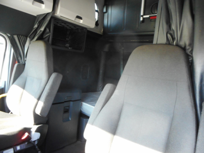 Cab interior of a Freightliner Cascadia 126 truck showing driver and passenger seats and a partial sleeper area.