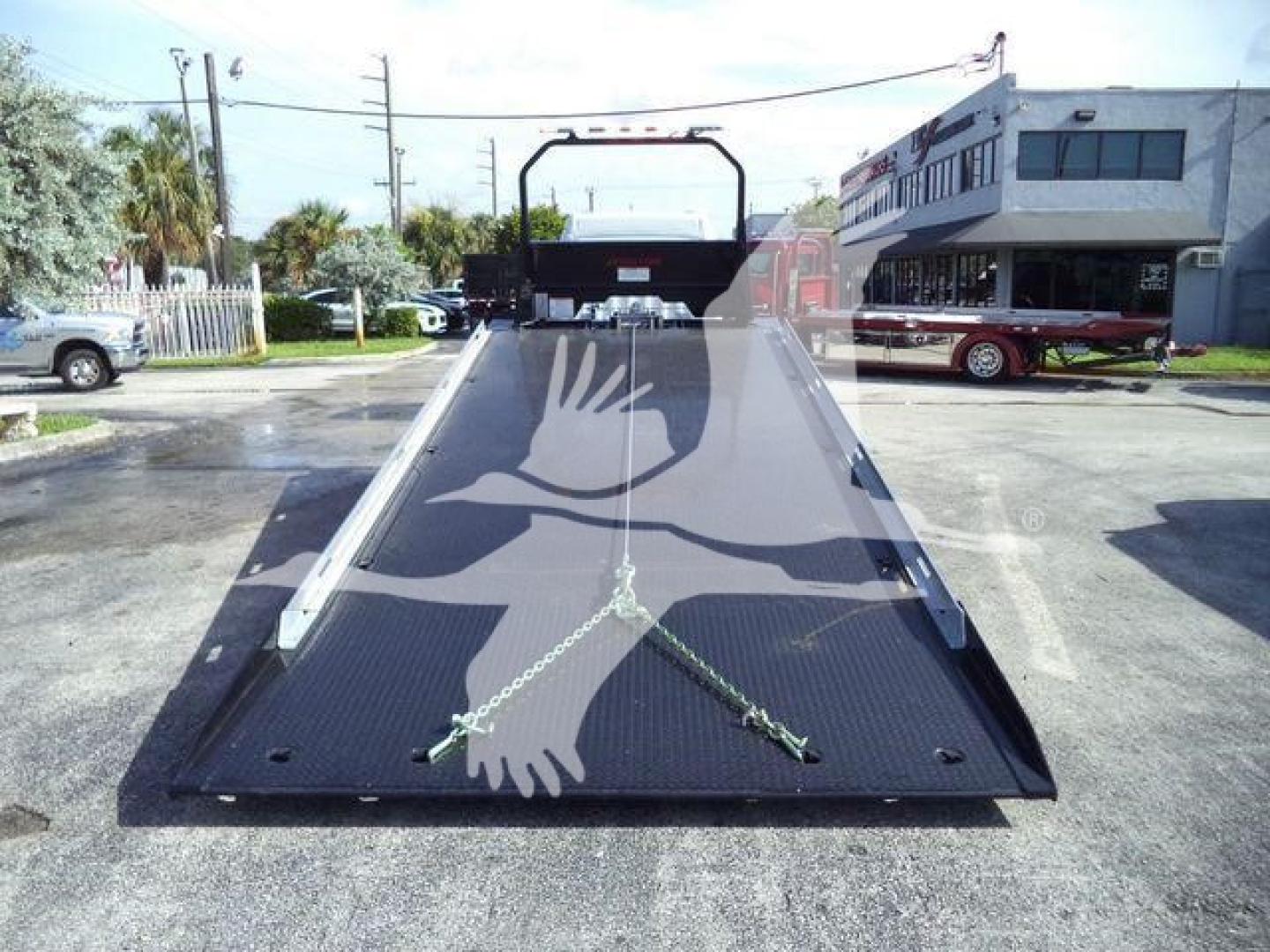 Truck flatbed towing equipment viewed from front, with ramp and handholds, in a dealership lot.