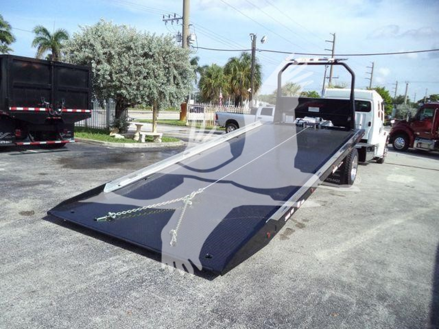 Freightliner Business Class M2 106 rollback truck with deployed flatbed ramp and wheel-lift bed in service bay.