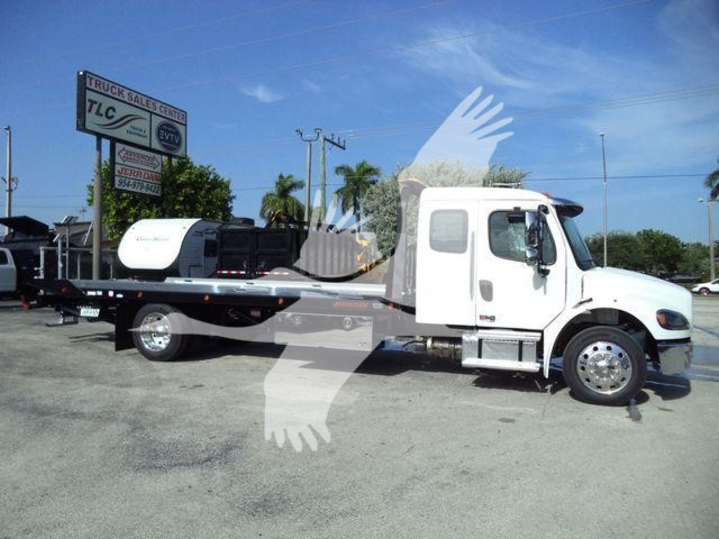 Freightliner rolling heavy-duty rollback tow truck side view showing cab and flatbed with wheel area and sign in background.