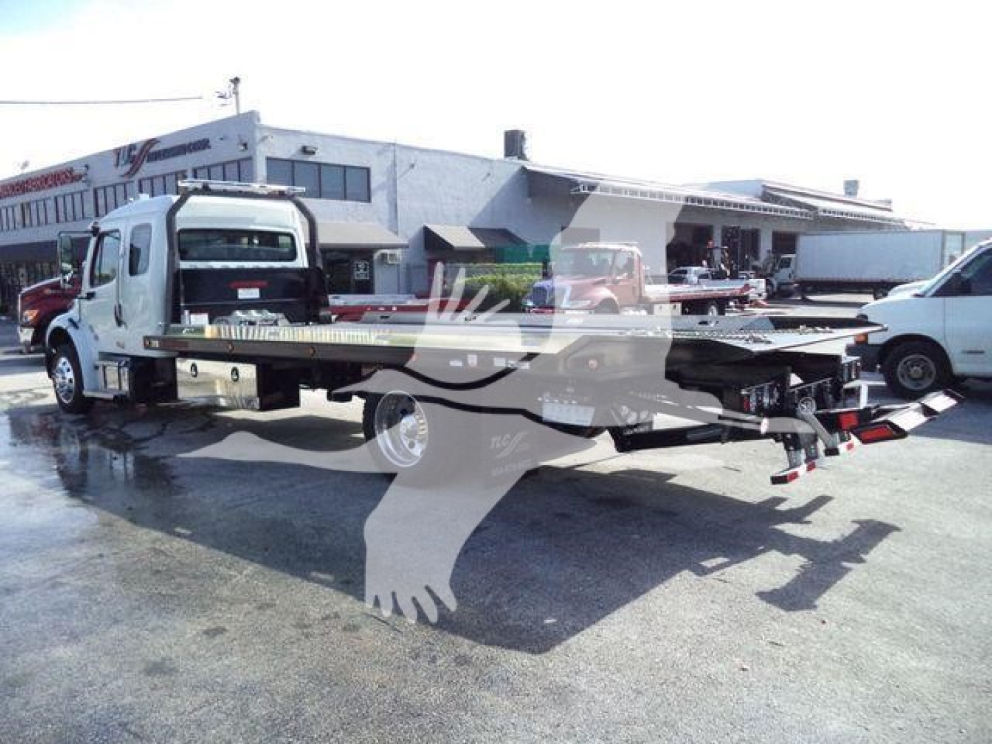 Freightliner Business Class M2 106 rollback truck with flatbed in a dealership lot, showing rear hitch and winch area.