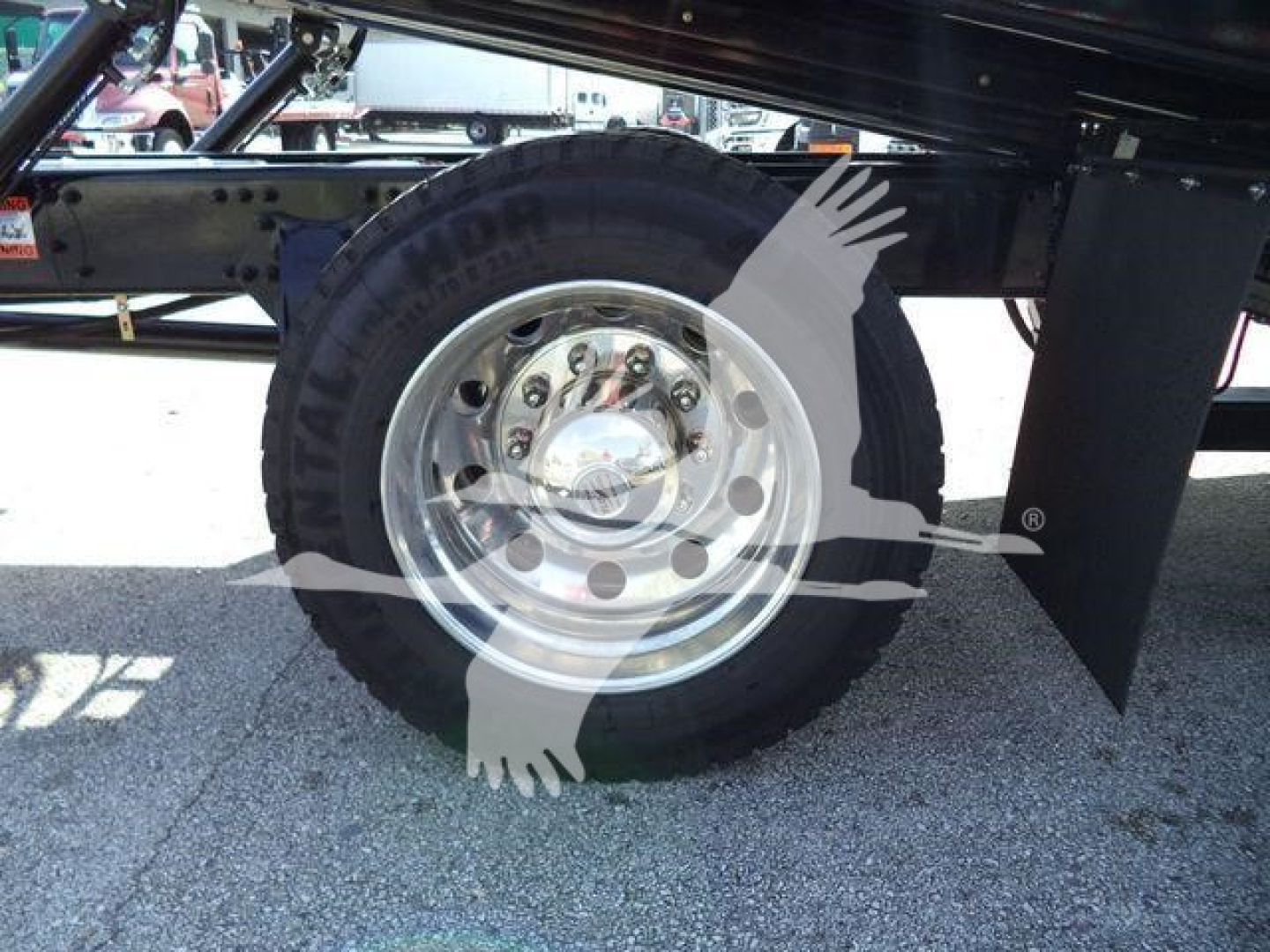 Freightliner Business Class M2 106 wheel and suspension with chrome hubcap and tire, showing part of frame and a watermark overlay.