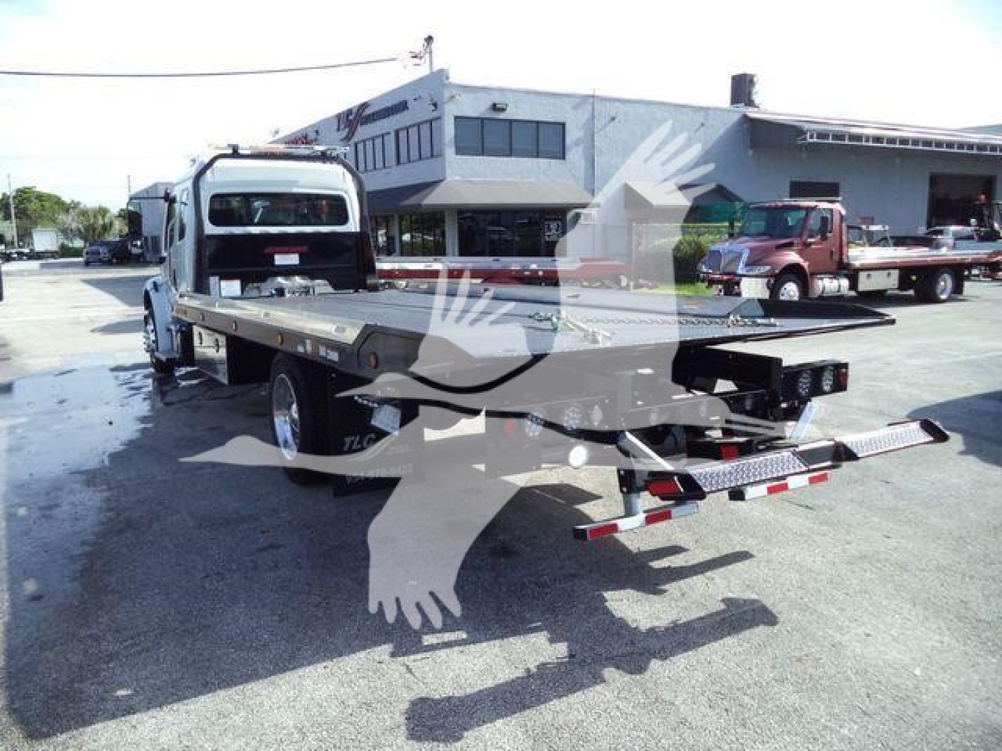 Flatbed tow truck with rollback bed on a Freightliner chassis in a dealership lot.