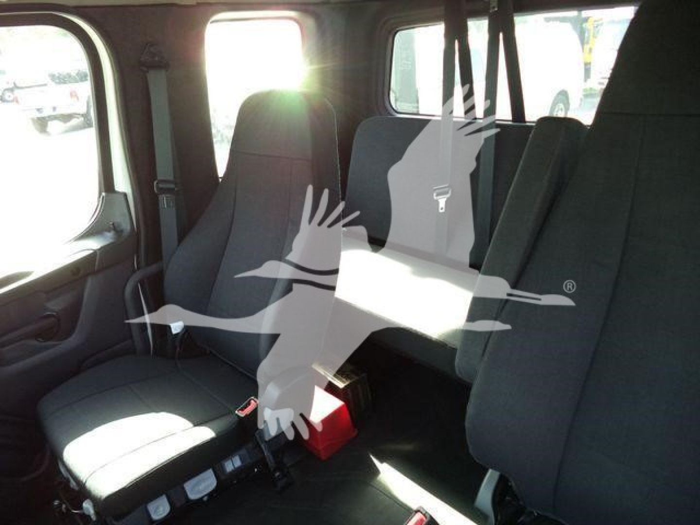 Freightliner M2 106 cab interior with seating for two and a folding jump seat, black fabric upholstery, daylight from window.