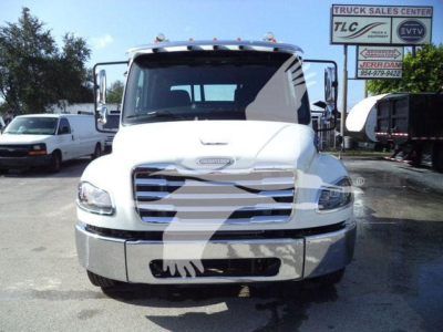 Freightliner Business Class M2 106 cab over front view showing chrome grille, headlights, and large bumper; dealership signage in background