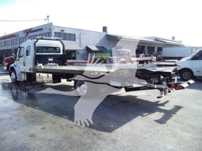 Freightliner Business Class M2 106 rollback truck with flatbed in a dealership lot, showing rear hitch and winch area.