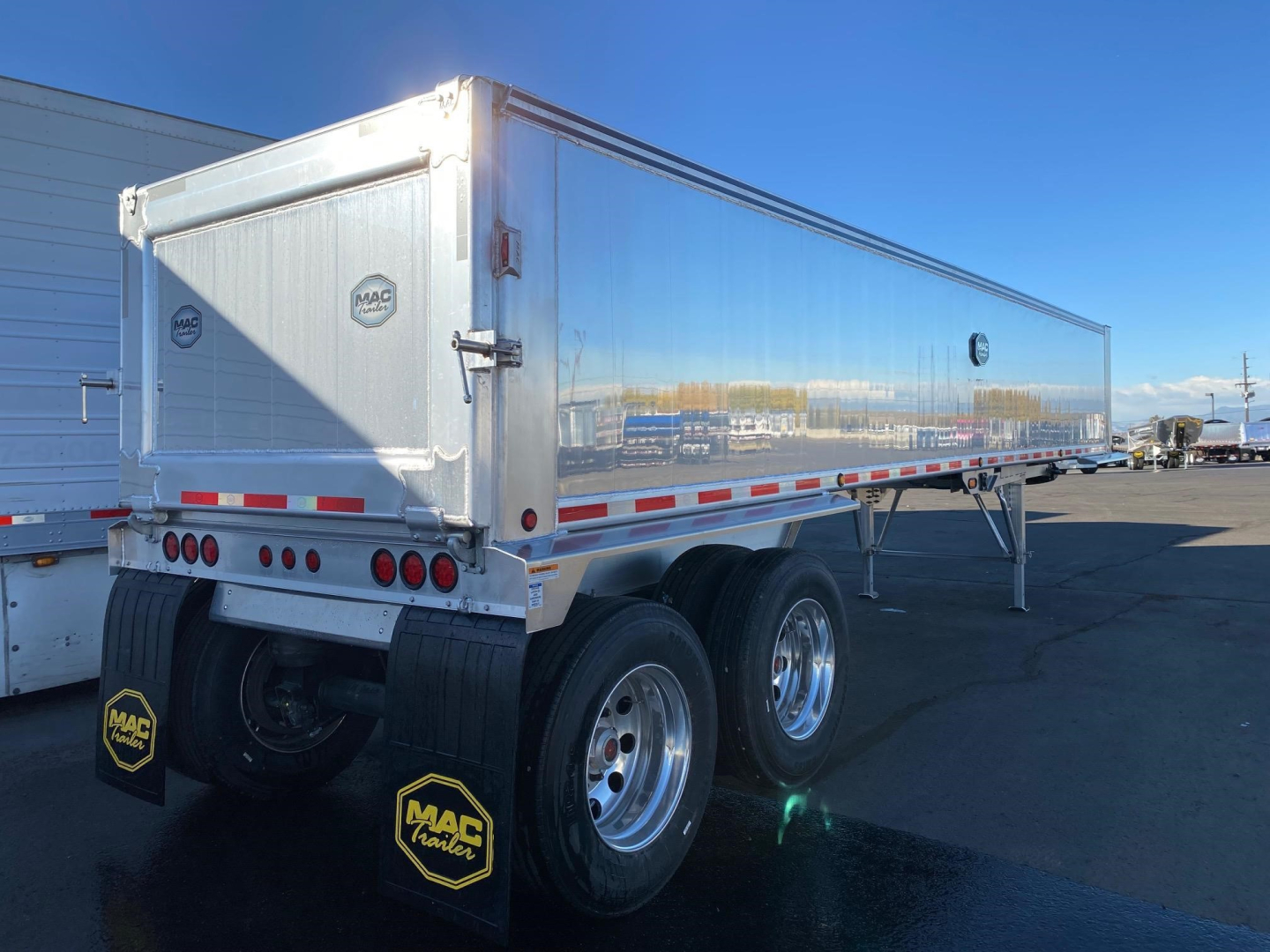 Mac Mac Western Lightweight dump trailer rear and side view showing dual rear axles, chrome wheels, aluminum body, tailgate with MAC logo, mud flaps, and reflective safety stripes.