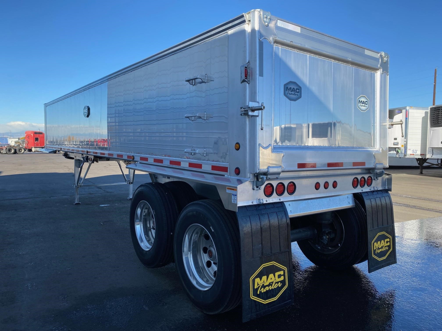 Rear-right view of a MAC trailer with galvanized aluminum sides, dual axles, mudflaps with MAC logo, rear doors, and taillights.