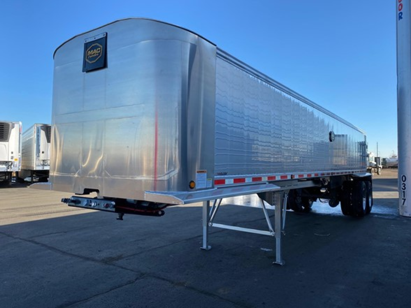 Aluminum trailer with elevated front legs and support braces, reflective sides, and a small Mac logo on the front left corner.