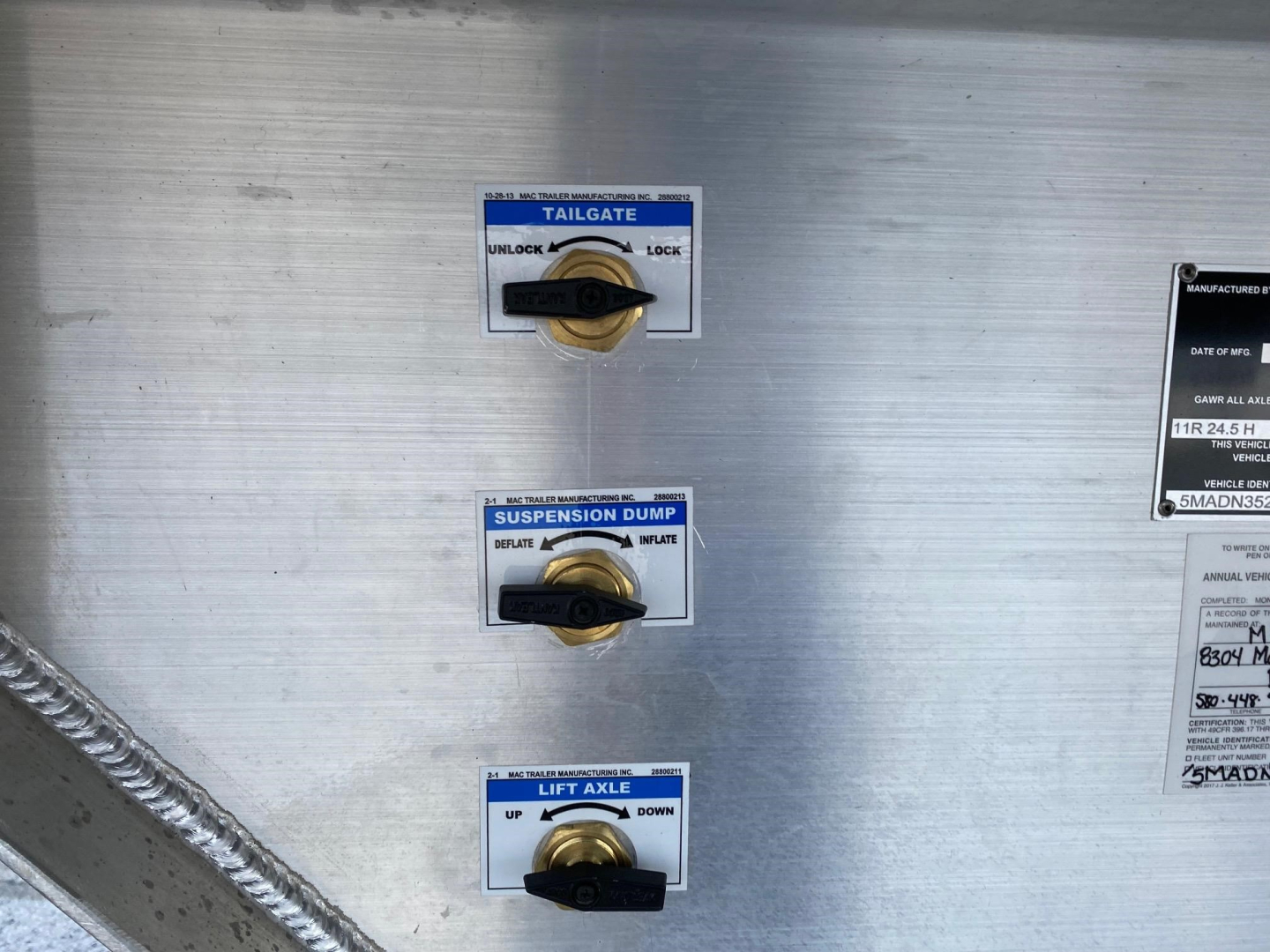Trailer equipment panel showing tailgate, suspension dump, and lift axle controls with labels and gold toggle levers on a metallic surface.