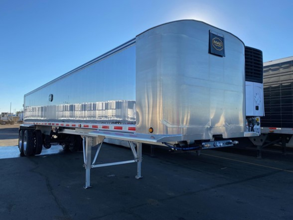 Trailer side view showing polished aluminum in-service dump trailer with M-A cornice logo on nose and support legs visible.