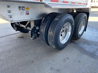 Dual rear trailer axle with spare wheel wells and undercarriage components visible; aluminum frame and tires on a Mac Western lightweight trailer.