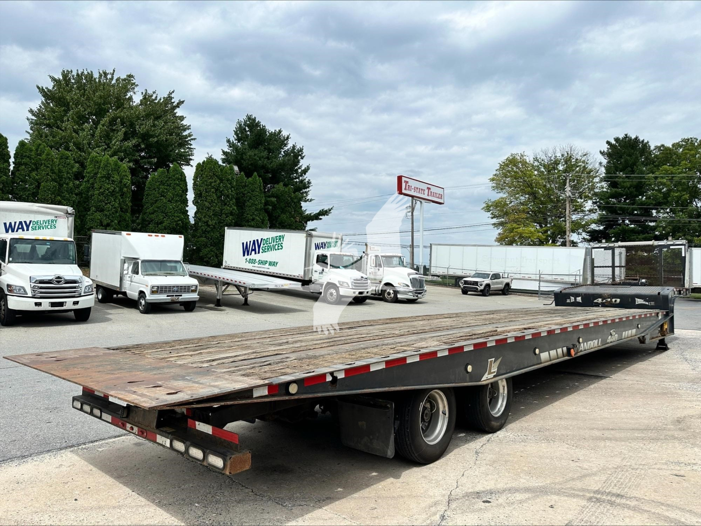 Trailer 2014 Landoll 440B platform trailer with dual rear axles and wooden deck; shows long flatbed and ramps; visible trucks and dealership yard in background.