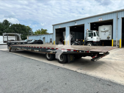 Landoll 440B trailer in a yard showing a long flatbed with dual rear axles and wheel ramps, warehouse buildings in the background.