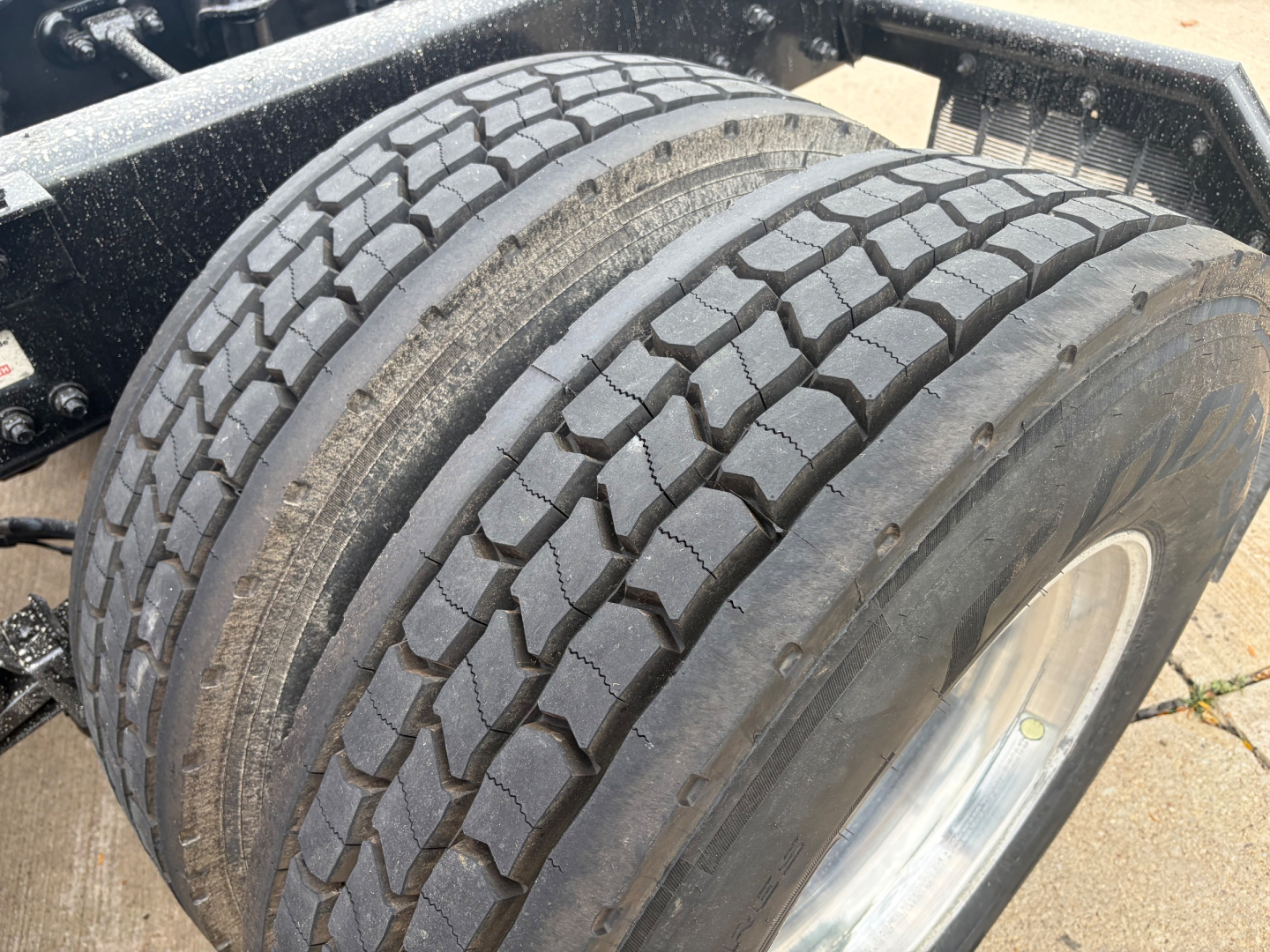 Kenworth T680 wheel/tire assembly showing dual rear tires with tread pattern and rim; part of truck chassis visible.