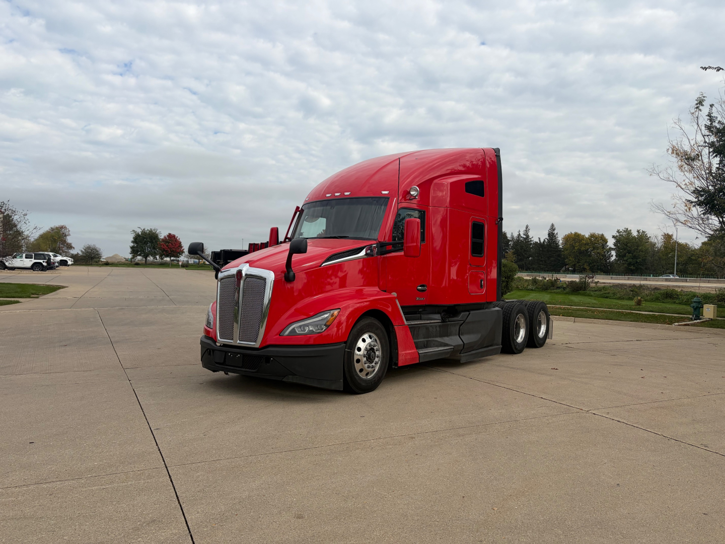 Kenworth T680 tractor in red color, front-left view, Sleeper cab, no visible damage, highway parking lot background