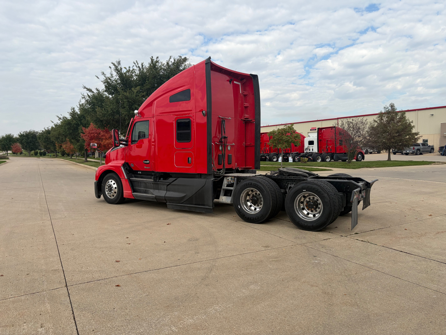 Kenworth T680 tractor in red with sleeper cab and exposed chassis, side view showing rear wheels and fifth wheel.