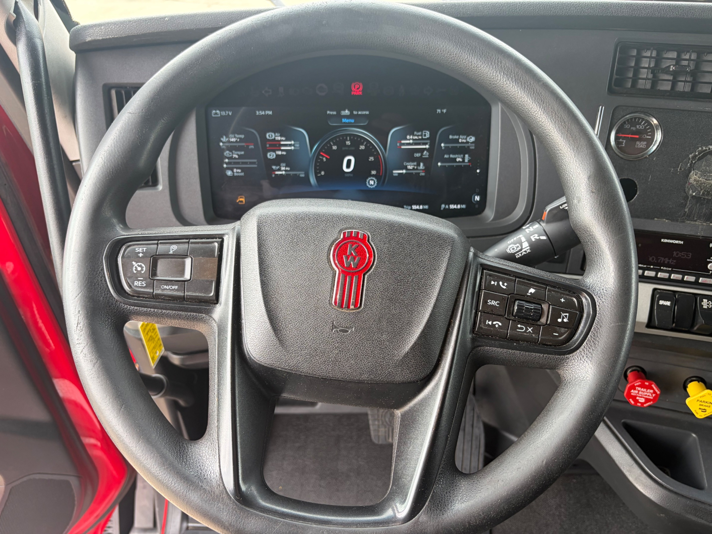 Kenworth T680 dashboard and steering wheel with digital instrument cluster visible through steering wheel, showing steering wheel controls and interior switches.